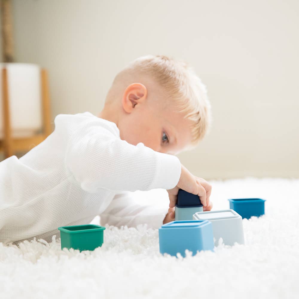 Front view of a child laying on the floor and playing with the Cool Blue Happy Stacks.