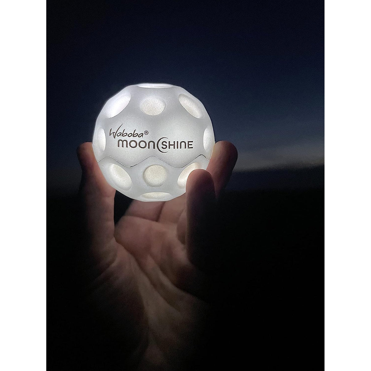 Front view of a person&#39;s hand holding a lit up Moonshine Ball.