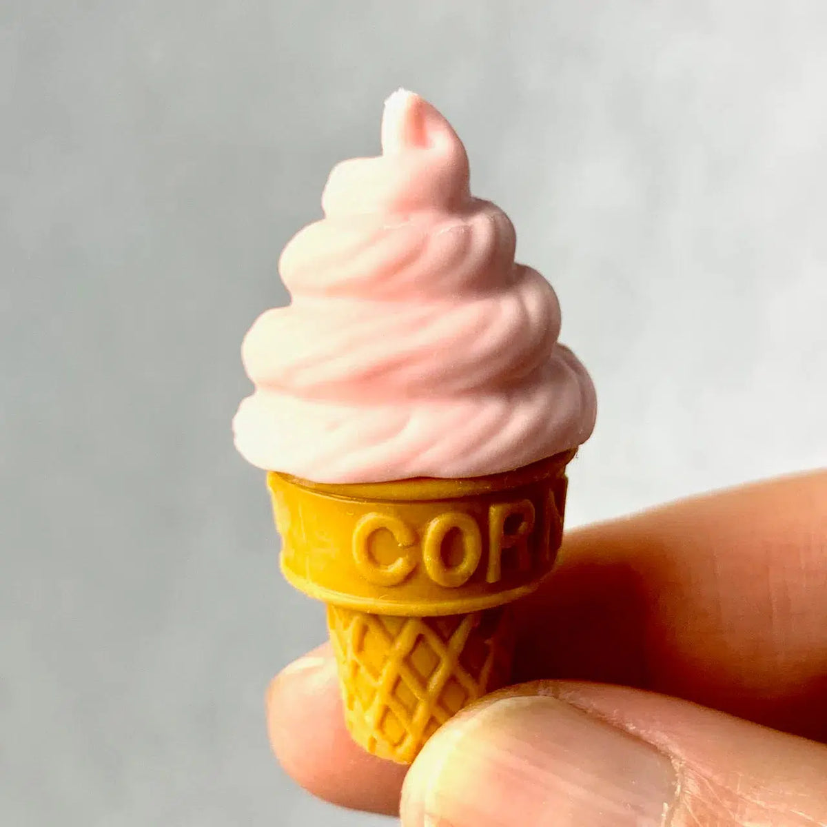 Front view of a person&#39;s fingers holding a peach colored Ice Cream Eraser.