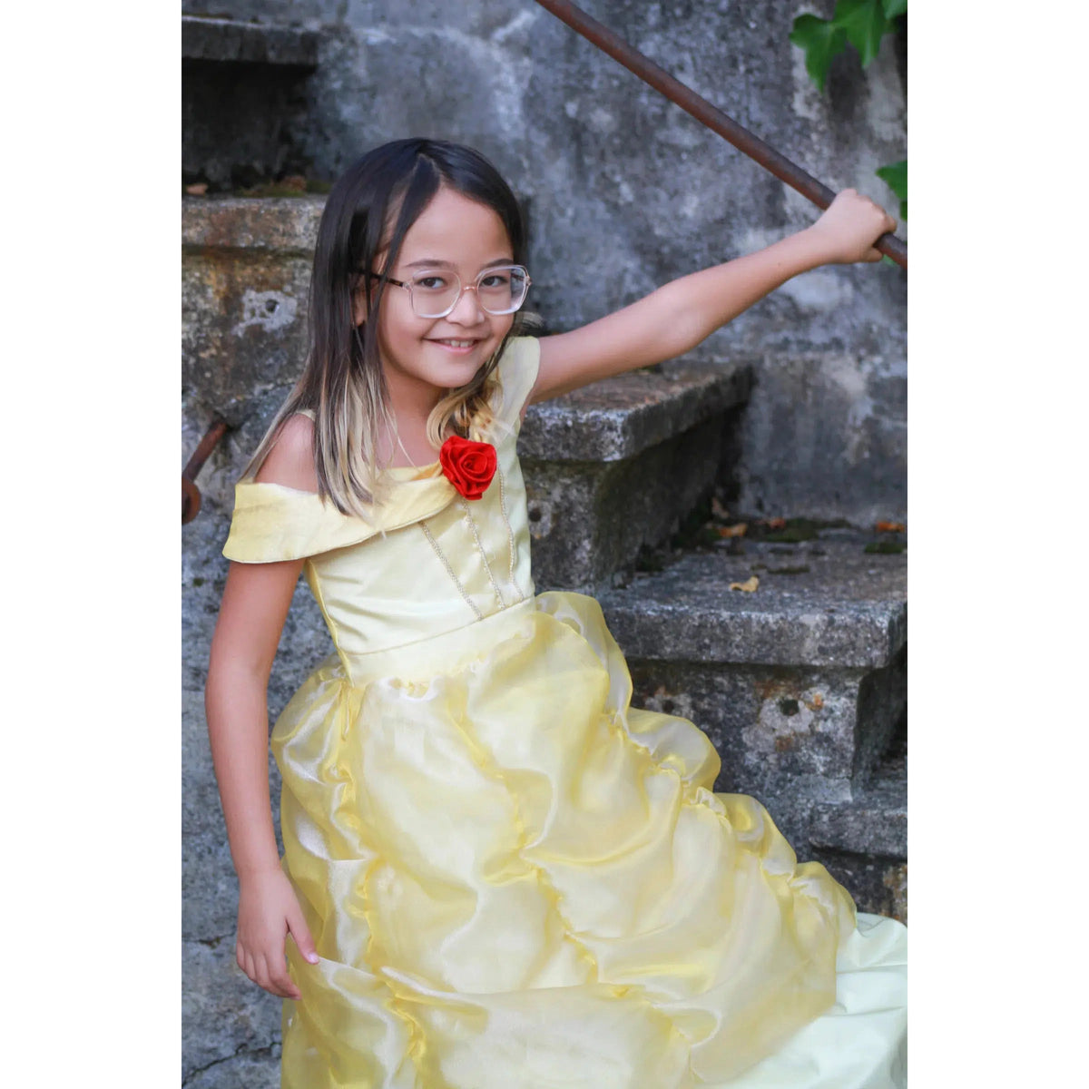 Front view of a young girl standing by steps in a Boutique Belle Gown.