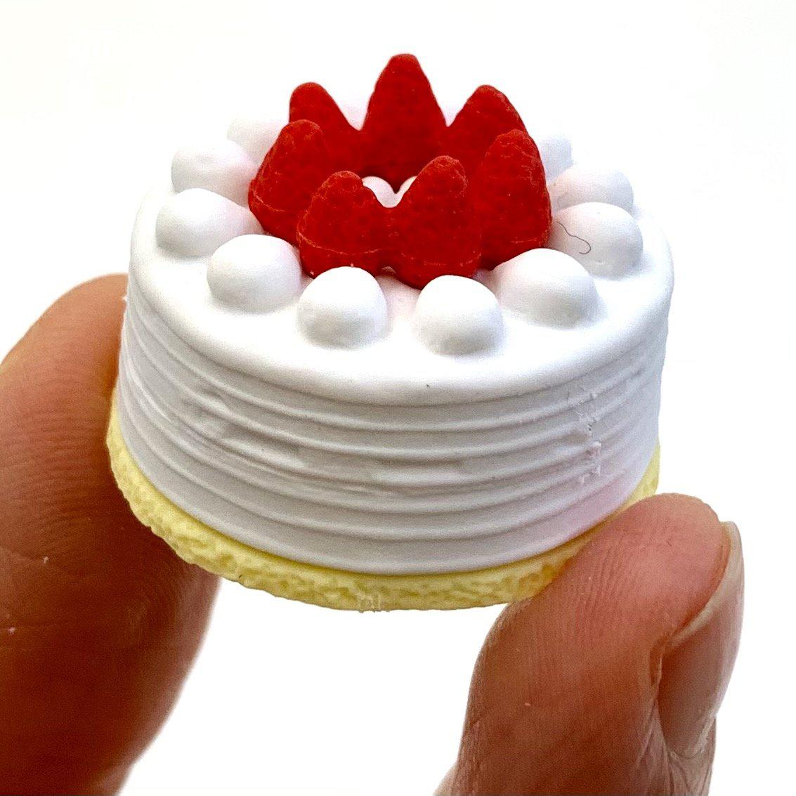 Front view of the white round cake with strawberries on top being held in someone&#39;s fingers from the Puzzle Eraser-Dessert.