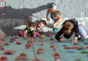 A view from above of a family climbing a rock wall, the father and son are looking directly up at the camera.