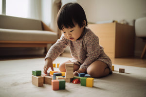 A young child kneeling on a carpet, playing with multicolored blocks.