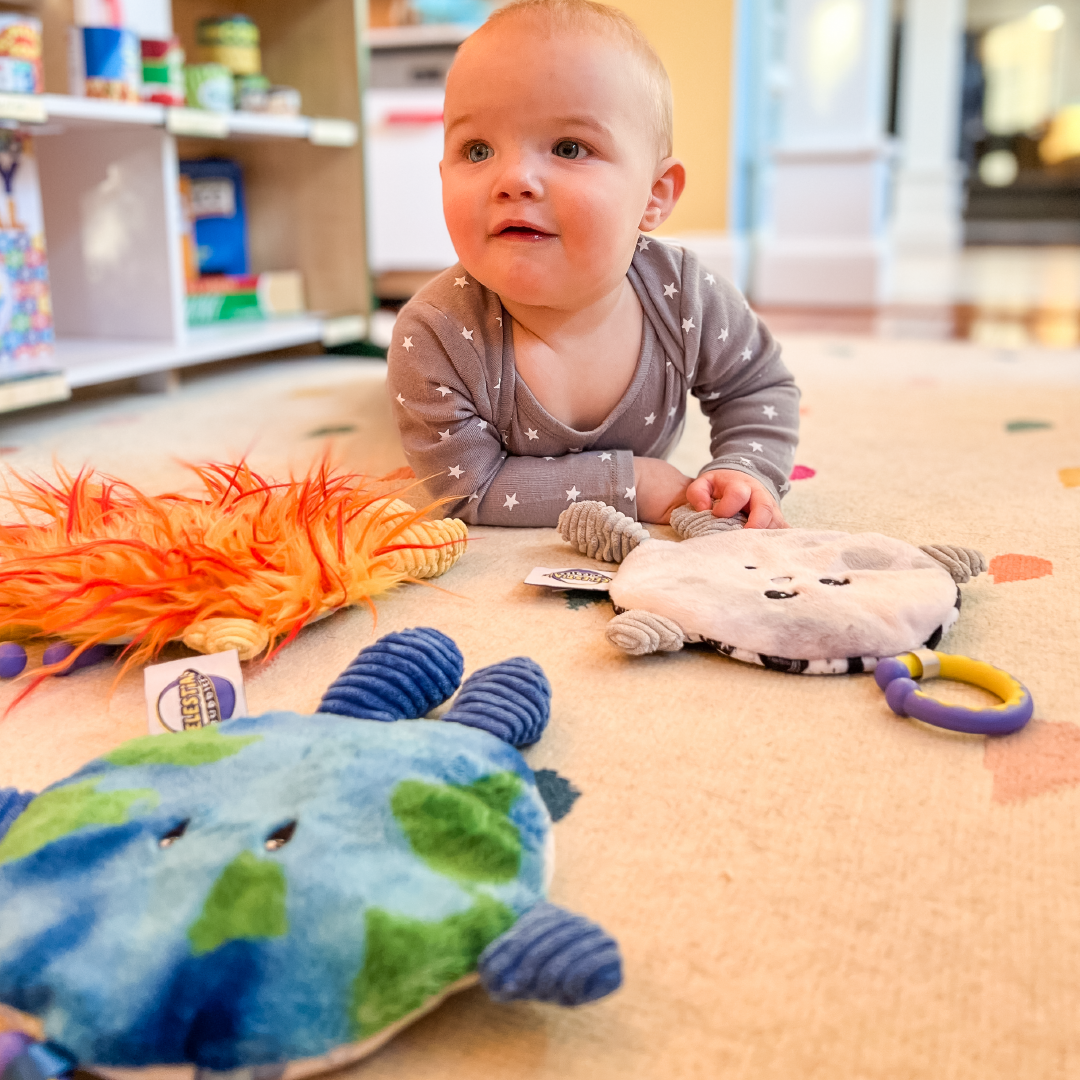 Front view of a baby laying on the floor with the Crunch Bunch Moon and other toys laying in front of the baby.