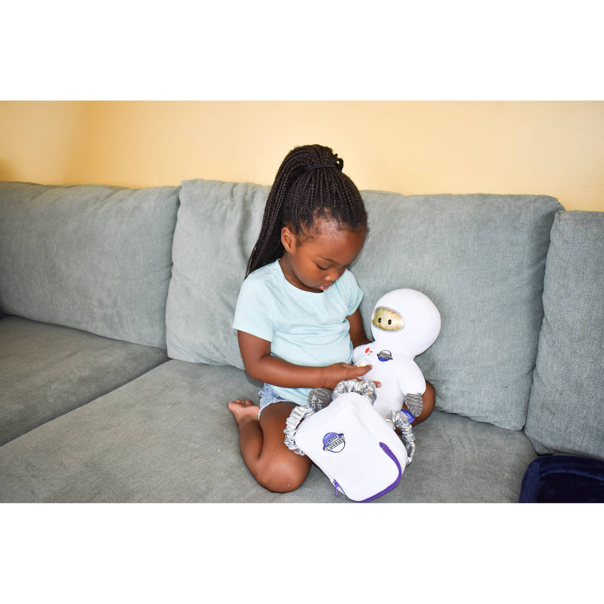 Front view of a young girl sitting on a couch playing with the AstroBuddy.