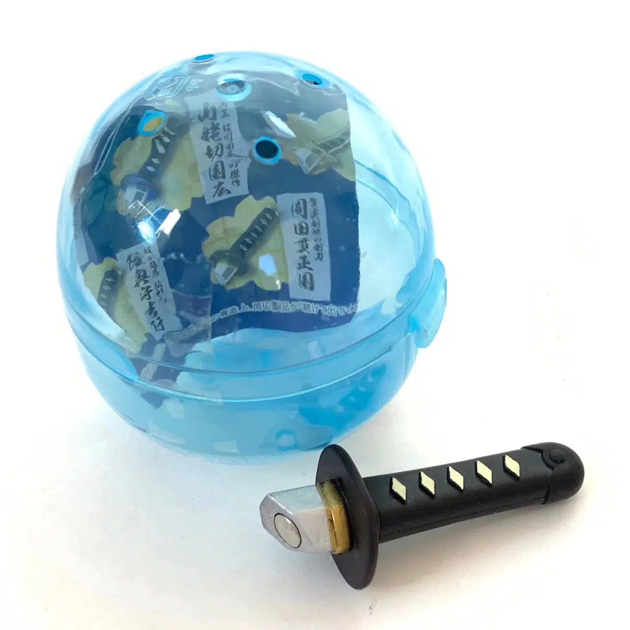 Front view of blue capsule with black and gold Samurai Katana Sword Magnet Capsule.