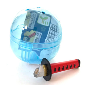 Front view of blue capsule with red and black sword from the Samurai Katana Sword Magnet Capsule.