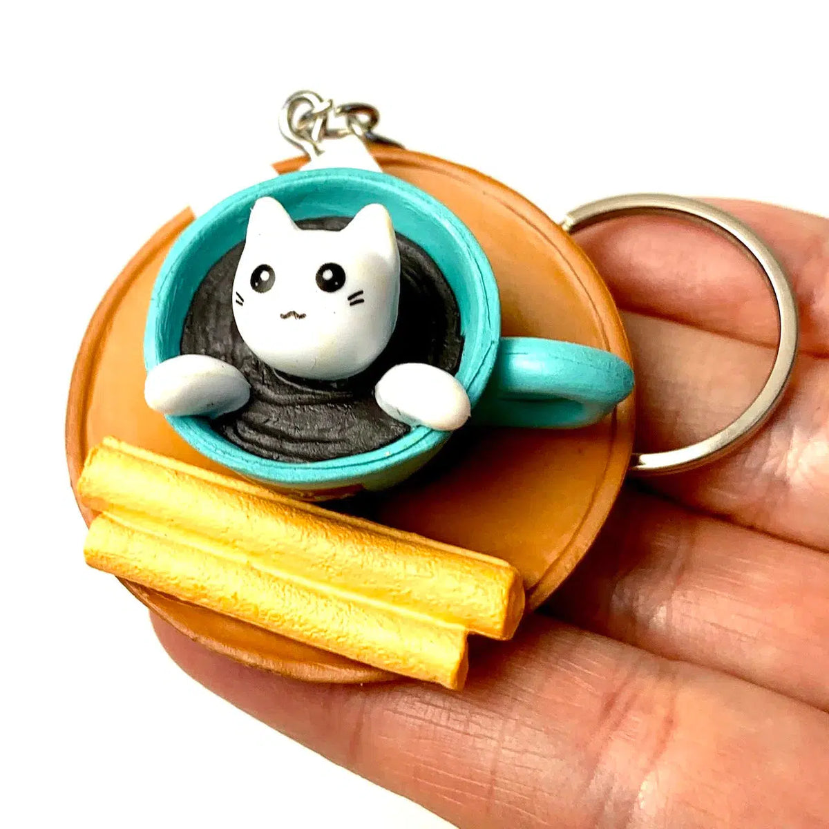 Front view of a person&#39;s hand holding the white cat in a turquoise coffee cup from the Key Charm-Cat Cafe.