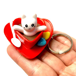 Front view of a person holding the white cat Key Charm -Cafe sitting in a heart shaped coffee cup.