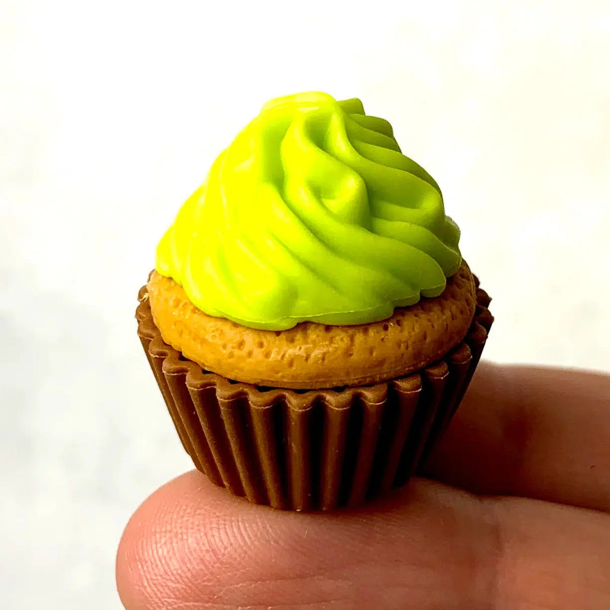 Front view of a person&#39;s fingers holding the yellow cupcake with green frosting from the Puzzle Eraser Card Set-Dessert.