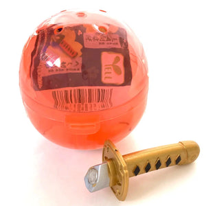 Front view of the red capsule with gold and black sword from the Samurai Katana Sword Magnet Capsule.