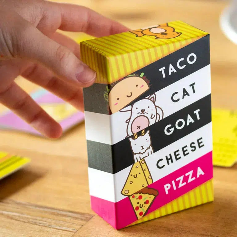 Front view of a person&#39;s hand holding up the Taco Cat Goat Cheese Pizza Game in its box.