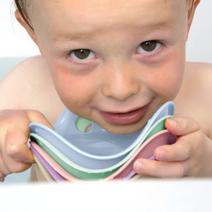 Front view of a baby in a tub holding a stack of the Bilibo Mini 6 Color Pack Pastels under their chin.