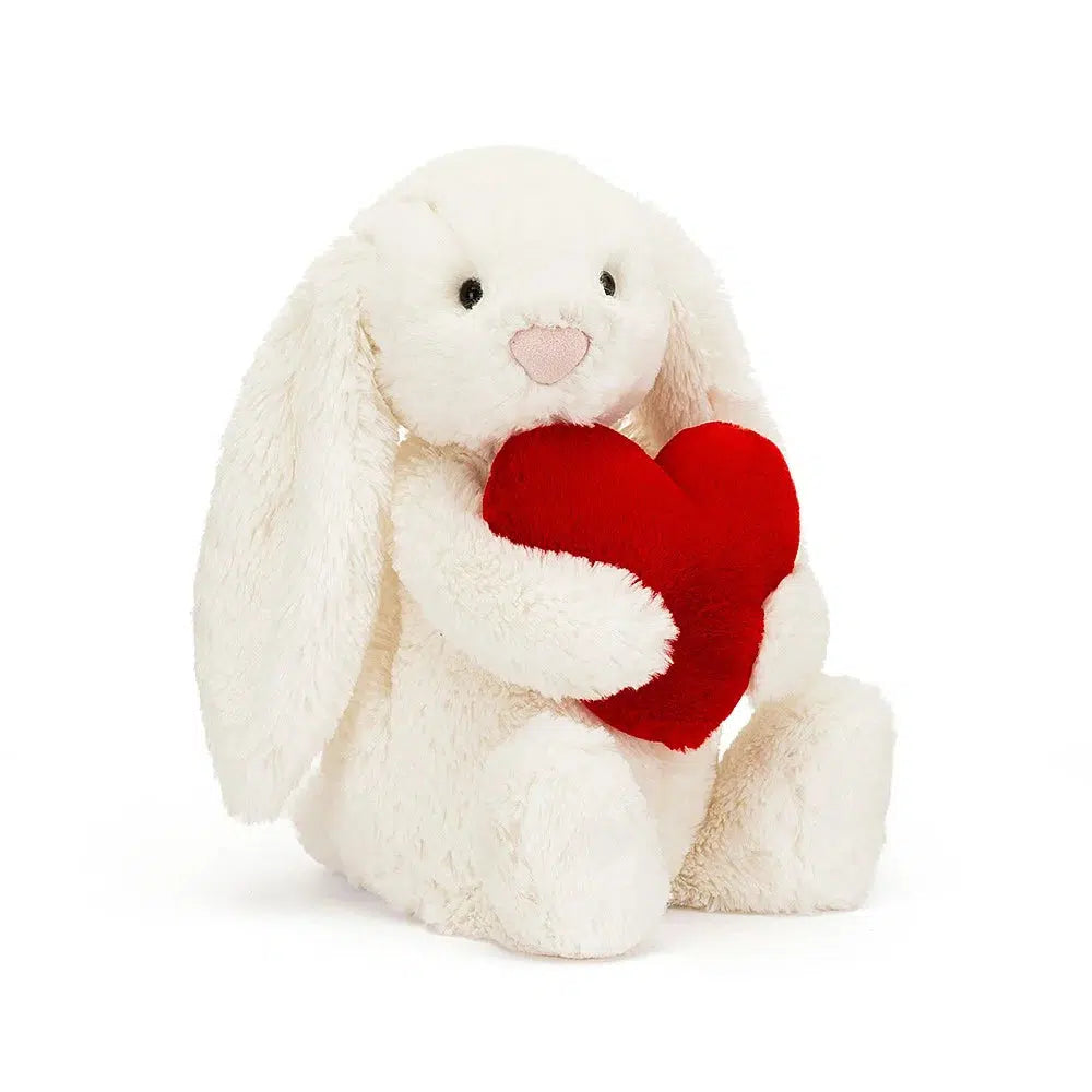 Front slightly side view of the Jellycat Bashful Red Love Heart Bunny 12&quot; holding the red heart.