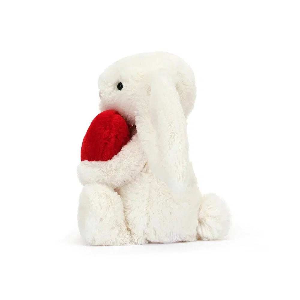 Left side view of Jellycat Bashful Little Heart Bunny holding the red heart.