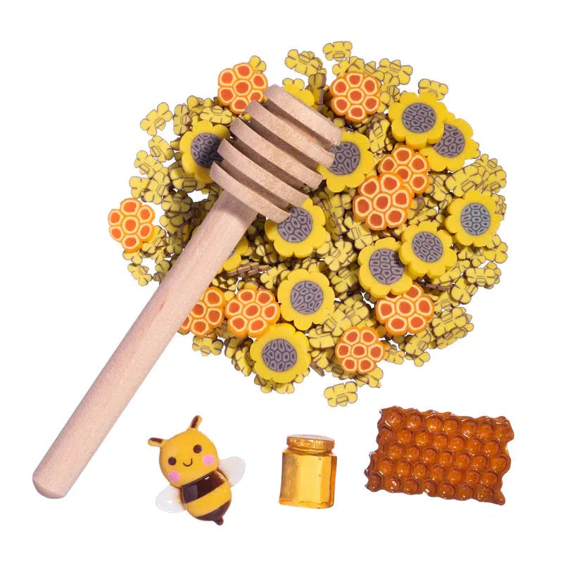 Front view of Sweeter Than Honey Slime Toppings out of package showing the contents: A honeystick, a honeycomb charm, a bee charm, a miniature honey jar, sunflower fimo slices, and honeycomb fimo slices.