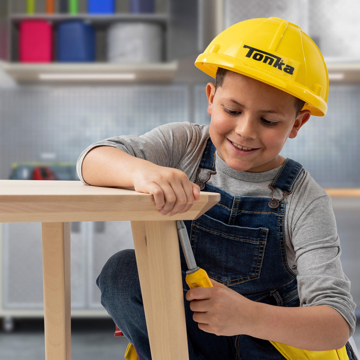 Front view of a young boy pretending to work on a table using a screwdriver and wearing the hat and tool belt from the Tonka Tough Tool Belt &amp; Hat Set.