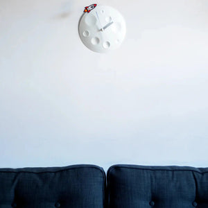 Front view of a Rocket Moon Clock hanging on a wall over a blue couch.
