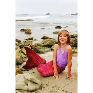Front view of a young girl sitting on the beach wearing the Fiji Red Mermaid Tail + Monofin Set.