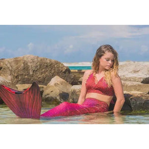Front view of a young woman sitting in water wearing the Fiji Red Mermaid Tail + Monofin Set.