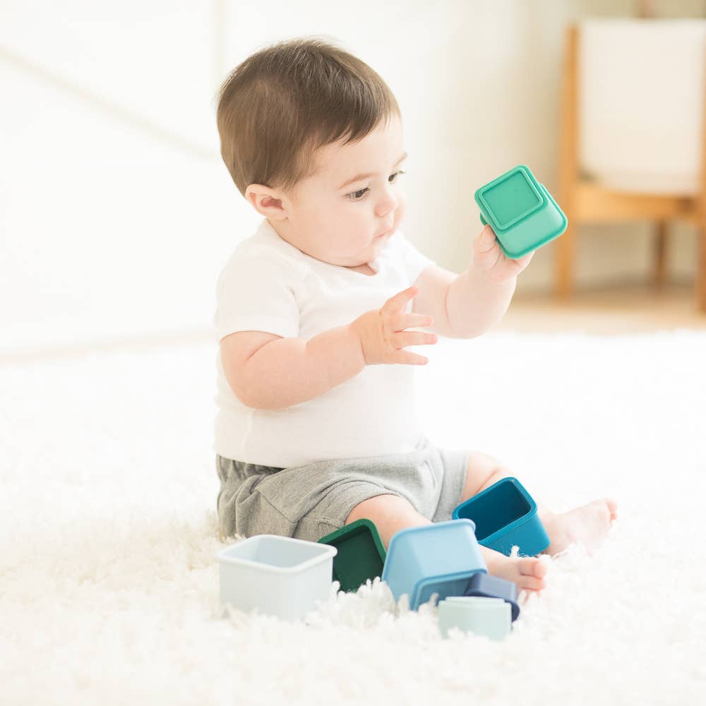 Front view of a baby holding one stack from the Cool Blue Happy Stacks with others on floor around him. 