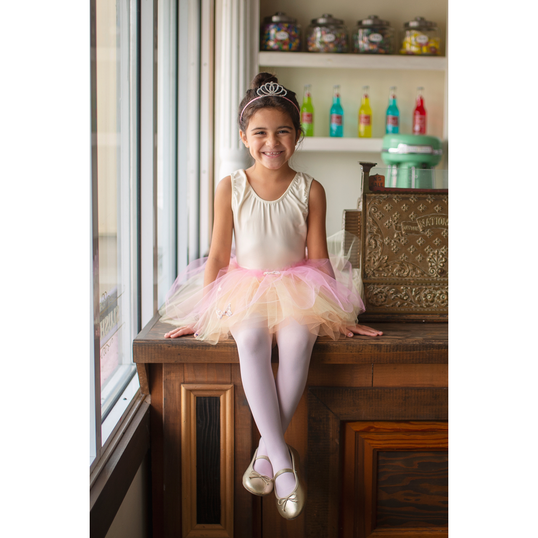 Girl with tiara and ballet shoes sitting on a counter wearing butterfly skirt