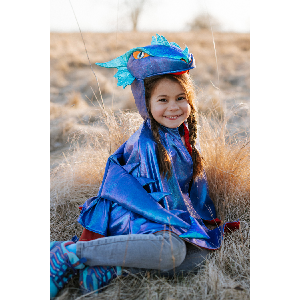 Girl seated in field wearing dragon cape and smiling