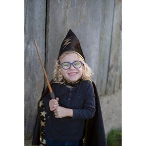 A smiling child with glasses, blonde ringlets, and a wizard had and cloak, holding the wand in two hands.