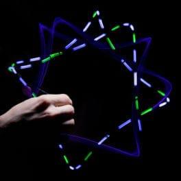 A hand holding the toy which has lights surrounding it. The lights have created four overlapping squares. Two of which are blue, the other two have both pink and green.