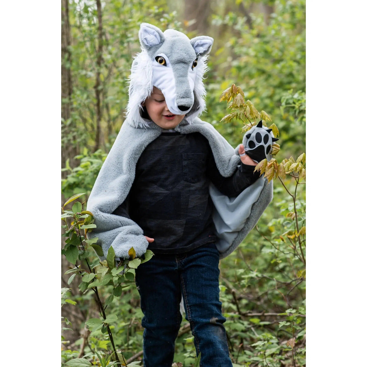Child in woods, wearing a grey and white wolf cape, walking and looking down.