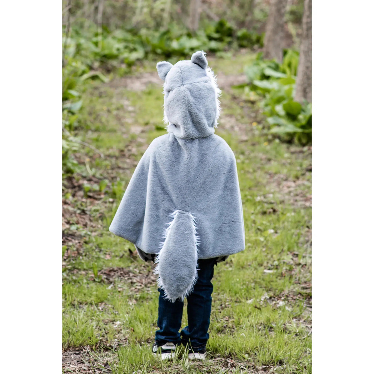 Child in woods, wearing a grey and white wolf cape, from behind.