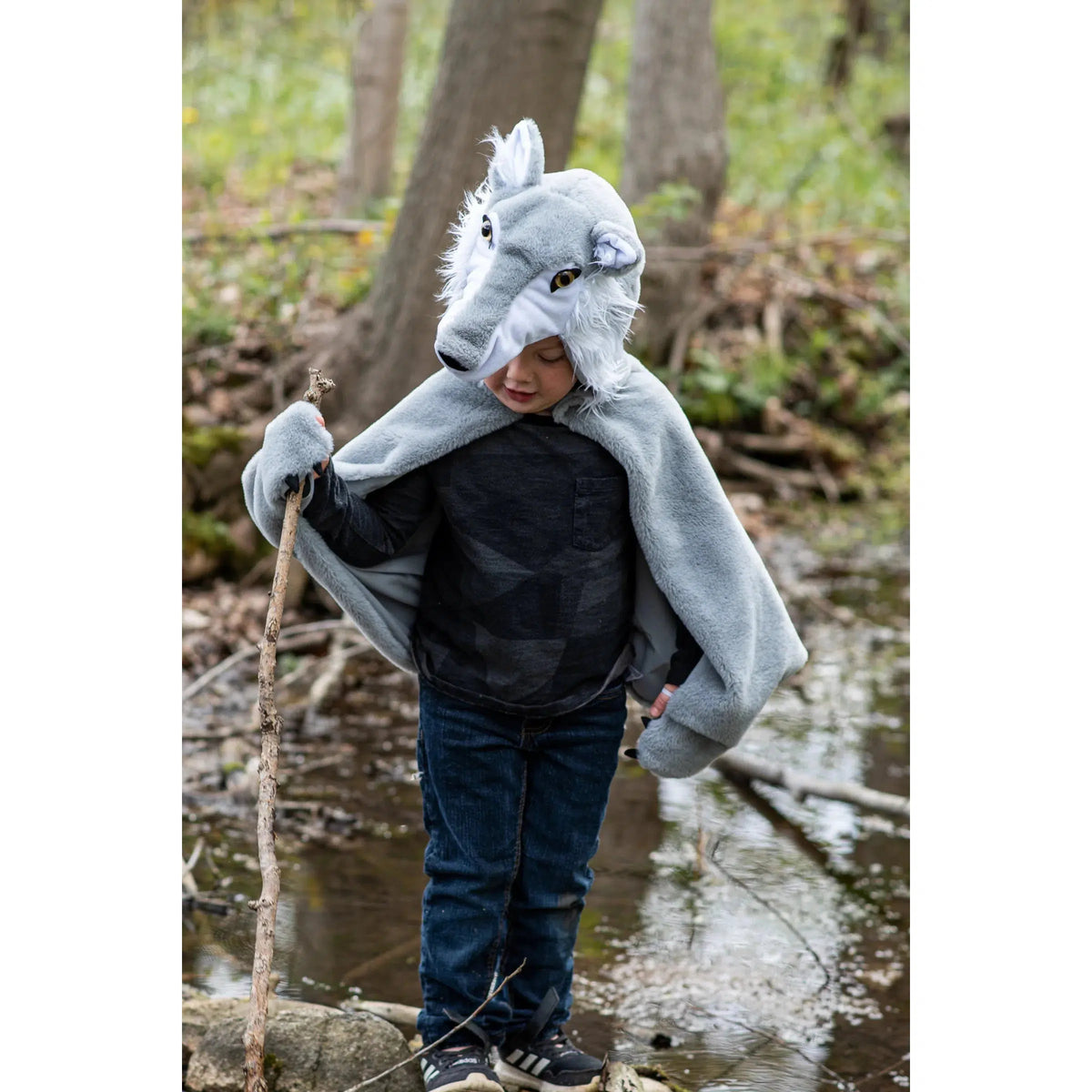 Child in woods, wearing a grey and white wolf cape, with a staff in a creek.