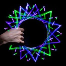 A hand holding the toy which has lights surrounding it. The lights have created six overlapping squares in green, blue, and purple