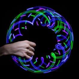 A hand holding the toy which has lights surrounding it. The lights have created six overlapping squares in green, blue, and purple