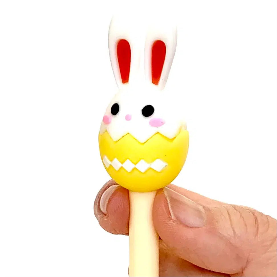 Front view of a person&#39;s fingers holding the yellow Bunny Egg Gel Pen at the top showing the yellow egg with the bunny head in it.