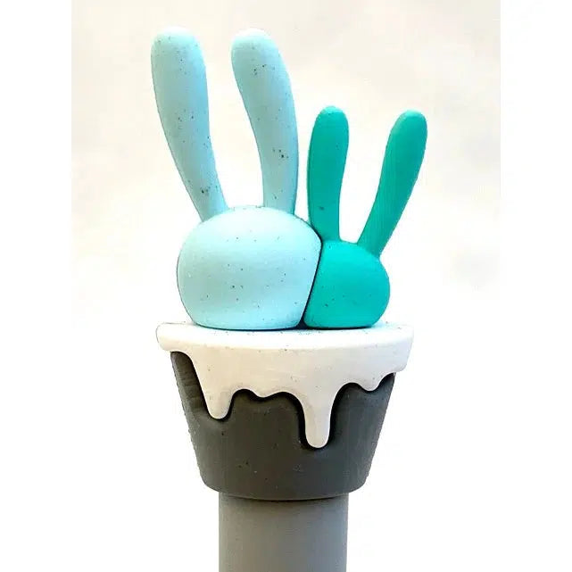 Front view of light turquoise and dark turquoise cactus in a black pot with white top sitting on a top of a gel pen.