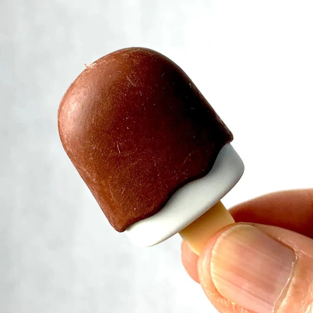 Front view of a person&#39;s fingers holding a chocolate Ice Cream Eraser.