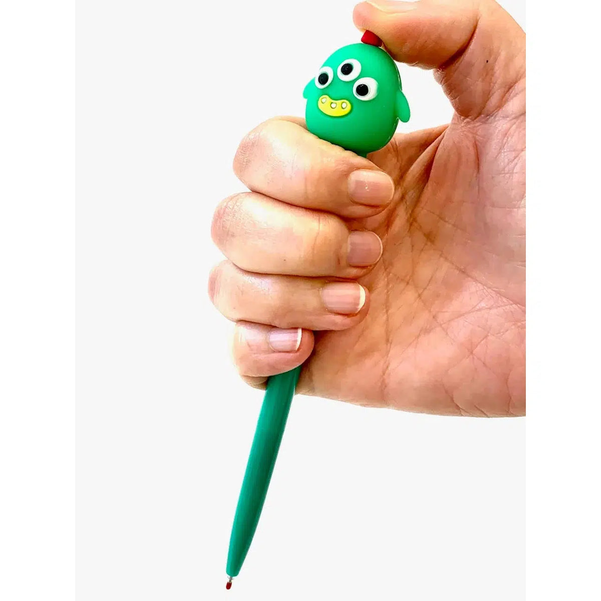 Front view of the dark green with three eyes monster being held in a person&#39;s hand with their thumb on top of the pen to click to write with the Cute Little Monster pen.