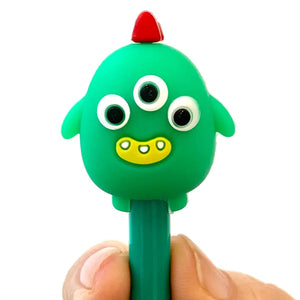 Front view of the green with yellow mouth and three eyes Cute Little Monster pen being held up by a persons thumb and finger.