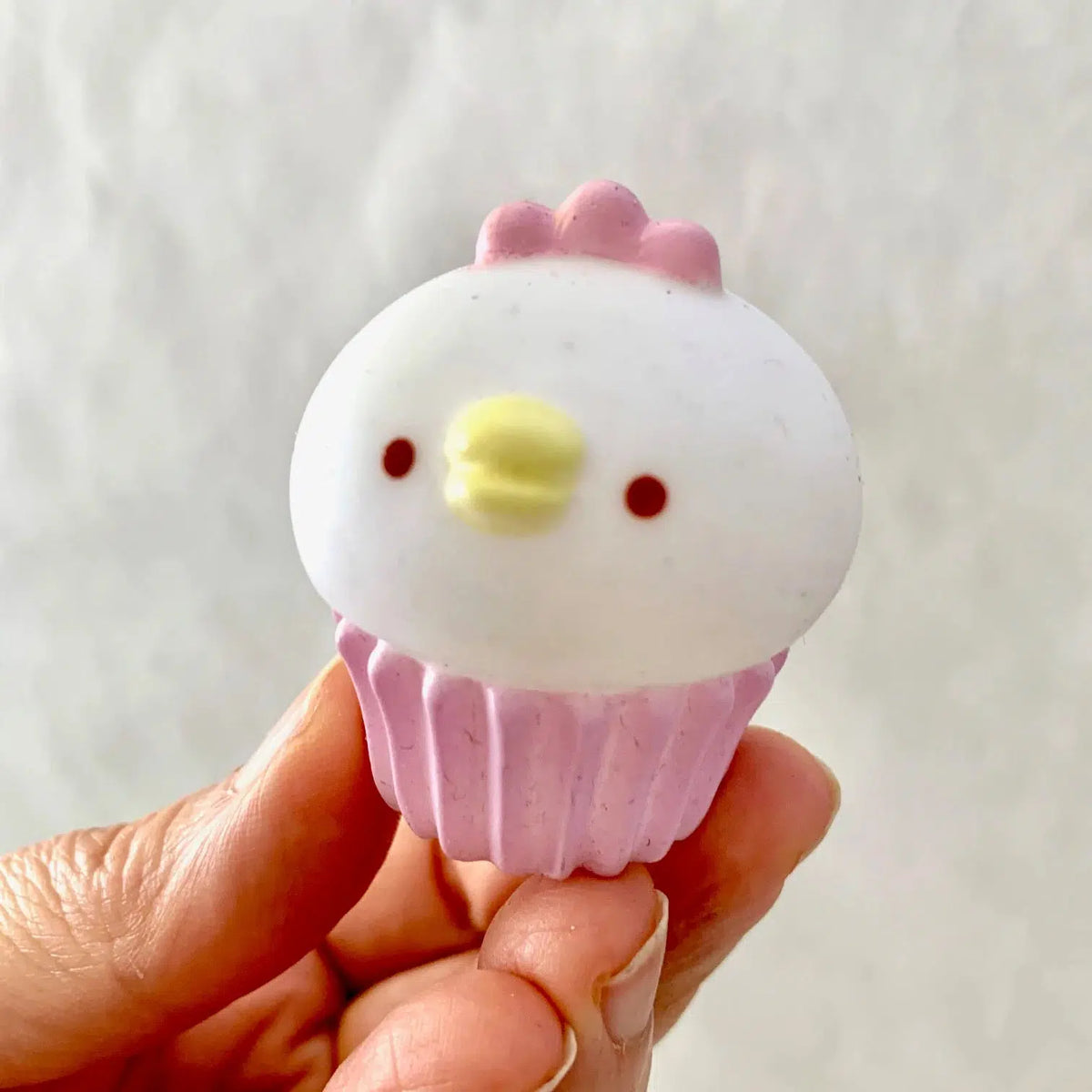 Front view of white chick sitting on pink cupcake tin in a person&#39;s hand.