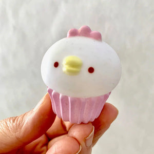 Front view of white chick sitting on pink cupcake tin in a person's hand.