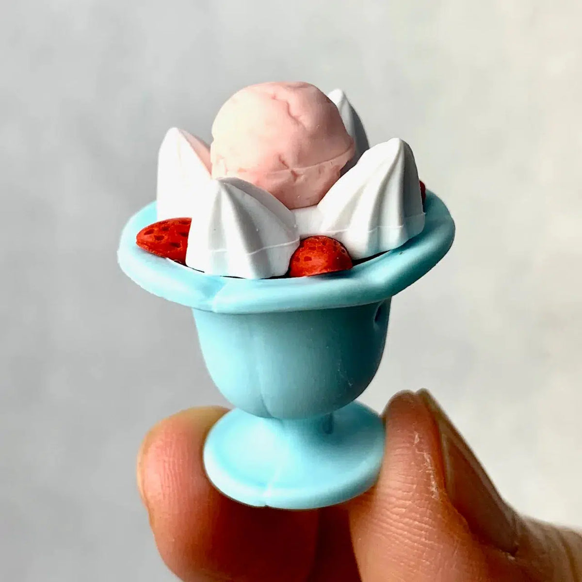 Front view of a person&#39;s fingers holding a strawberry sundae from the Ice Cream Erasers.