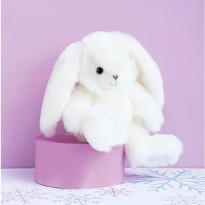 Front view of white dapper rabbit sitting on a lavender round box one foot hanging off with a lavender background.