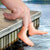 Front view of someones hand on a dock with two fingers dangling in water with Finger Puppet-Finger Feet on the fingers.