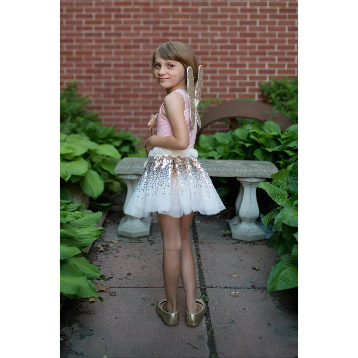 Front rear view of a little girl wearing the Gracious Gold Sequin Skirt with the wings and holding the wand.