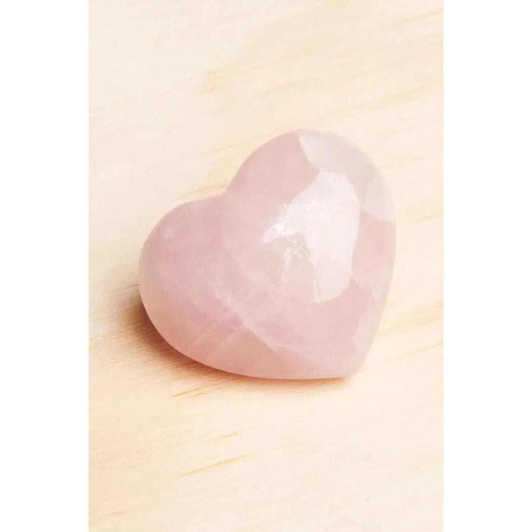 Front view of a Rose Quartz Heart laying on a wooden table.