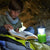 Front view of a boy sitting on a sleeping bag and reading a book with the help of the Terra Kids Camping Lantern.