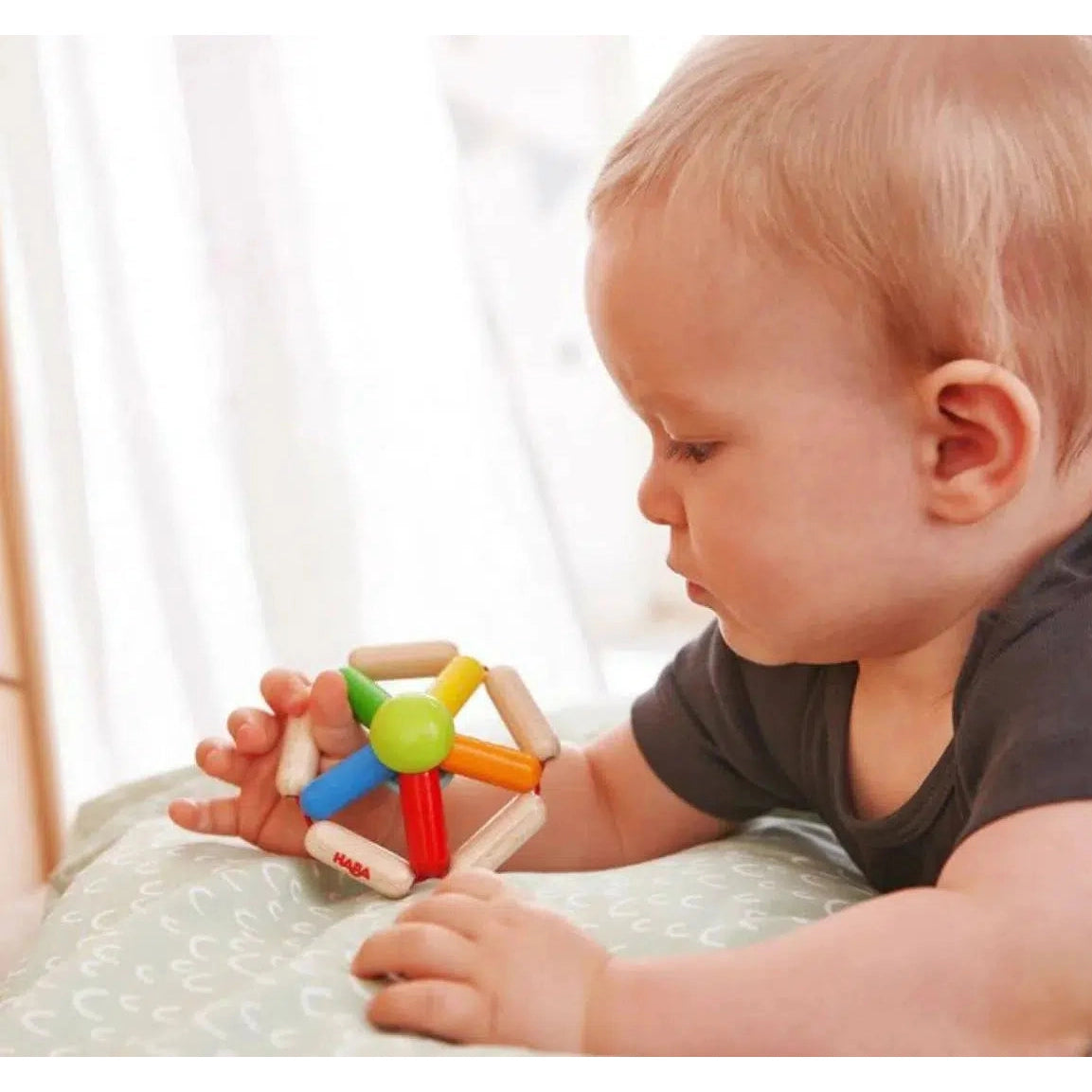 Front view of a baby holding and looking down at the Clutching Toy Color Carousel.