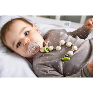 Front view of a baby with a pacifier in their mouth that is attached to the Pacifier Chain Star Flight.