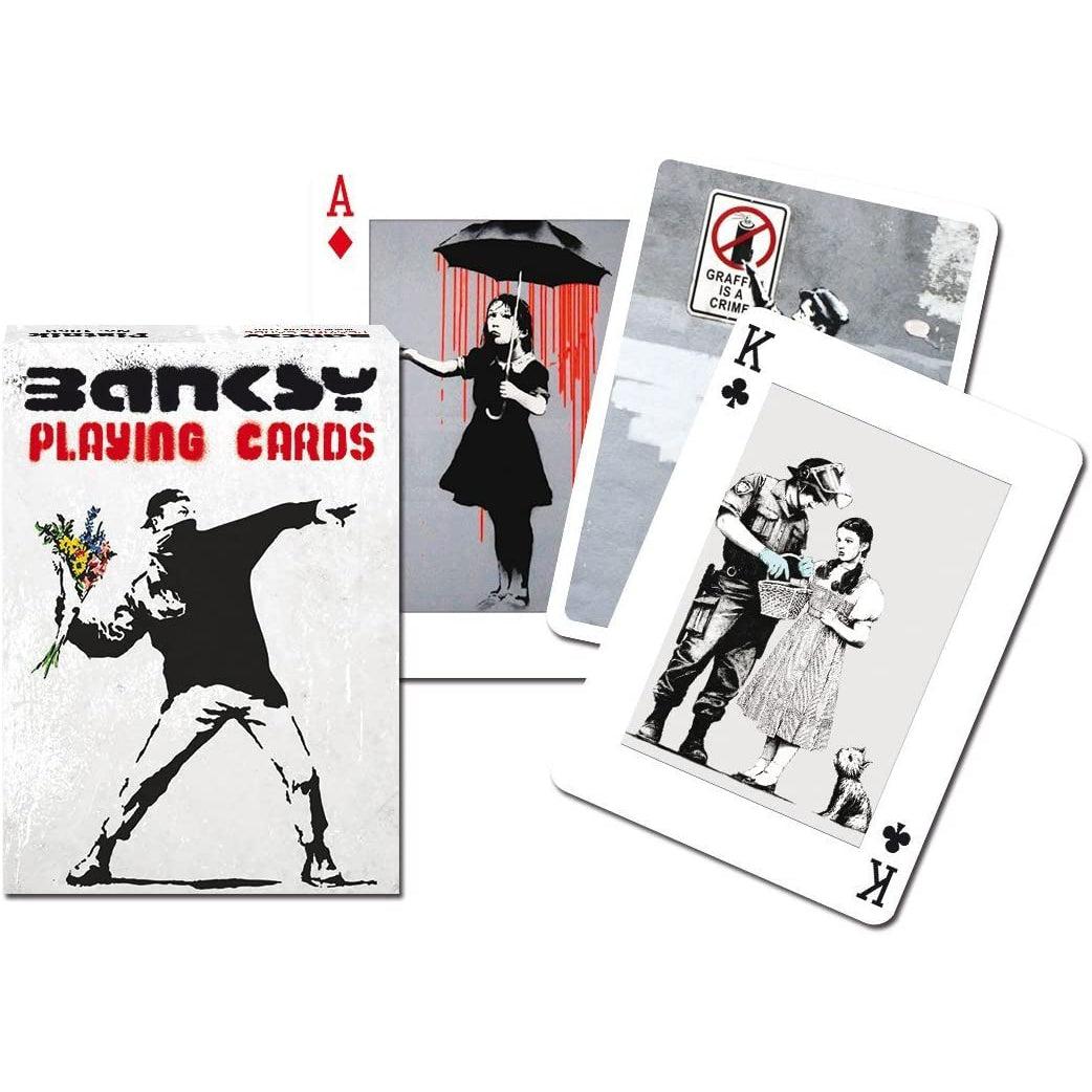 Front view of Banksy Playing Cards in its box and various cards beside it.